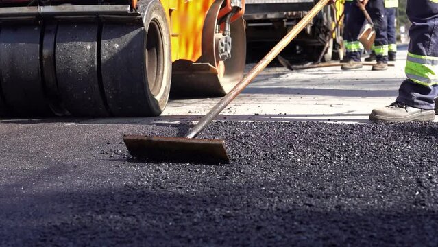 Worker Leveling Fresh Asphalt on a Road Construction Site  - Slow Motion Video. Road Roller Leveling Asphalt. Men Working On Tarmac Road Maintenance. Worker Using Asphalt Lute. Road Construction Works