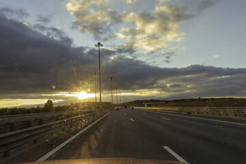 Traffic at dawn. The road with a metal safety barrier is illuminated by the morning sun.