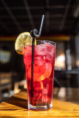 Red cocktail in a tall glass with ice, fresh berries and fresh mint on a wooden surface and on a solid black background, sprinkled with freshly squeezed pomegranate juice