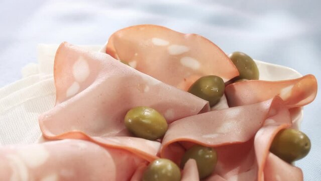 slices mortadella with olives on a white plate. Italian sausage on a table with a blue surface. serving meat delicacy. traditional boiled sausage under sunlight.