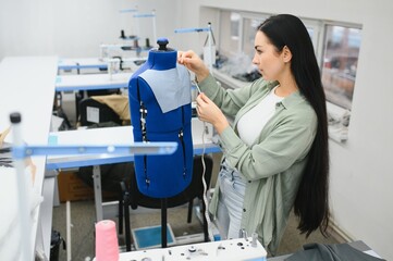 Positive young woman sewing with professional machine at workshop.