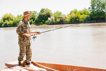 Thoughtful man in camo apparel standing at stern of boat, fishing in morning. Side view of male...