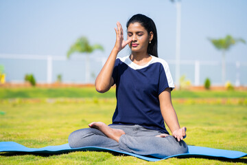 Young girl doing nostril breathing exercise or pranayama yoga with closed eyes at park - concept of self care, mindfulness and active morning routine. - obrazy, fototapety, plakaty
