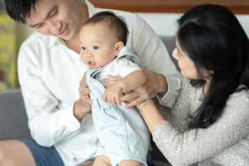 Father's Day concept, young Asian father holding a baby child with family person at home, happy childhood with love and care together, little cute son with dad and parent, parenthood lifestyle