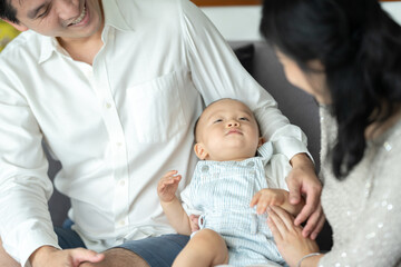 Father's Day concept, young Asian father holding a baby child with family person at home, happy childhood with love and care together, little cute son with dad and parent, parenthood lifestyle