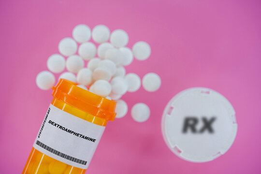 Dextroamphetamine Rx medicine pills in plactic vial with tablets. Pills spilling   from yellow container on pink background.