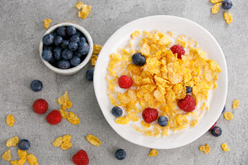 Tasty corn flakes with blueberries and raspberries in a black bowl, top view