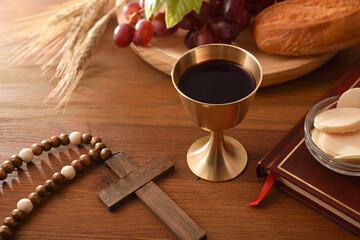 Wine glass and consecrated hosts on wooden table