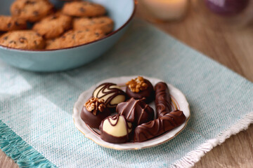 Plate of chocolate pralines, bowl of cookies, cups of tea, glasses of juice and lit candles on the table. Selective focus.