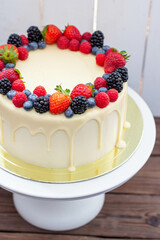 Cheesecake with fresh strawberry, raspberry, blueberry and blackberry, melted white chocolate on rustic wooden cakestand and background