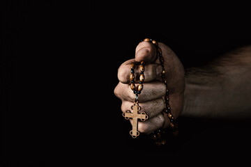 Dirty male hand holding a wooden cross on a black background