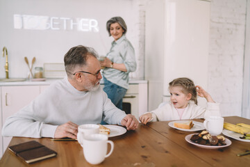 Grandfather and kid having breakfast in kitchen near grandmother