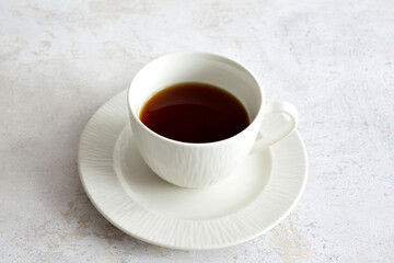 A white cup of coffee on a white saucer isolated on grey background, close-up