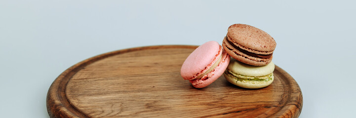 Three confectionery, sweet macaroons on a round wooden tray, macro isolated on a blue background. Banner for website header design with copy space.
