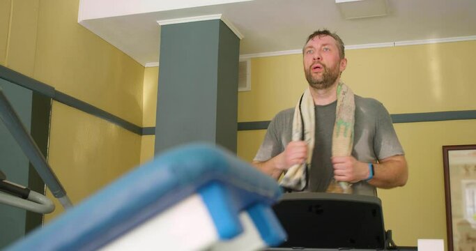 Middle-aged man with a towel on his neck runing on a treadmill. Slow motion video.