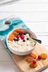 Fresh cottage cheese with dried fruits and berries in a white bowl on a wooden board.