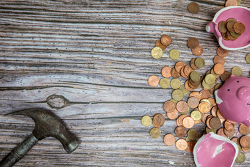Broken piggy bank smashed into pieces with hammer, with cash and coins on wooden background top view with copy space, money savings concept