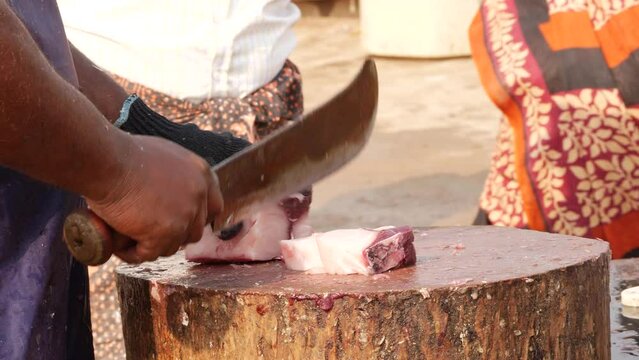 A man using a cutlass to cut a big fish part into five pieces, a woman fetching at the background