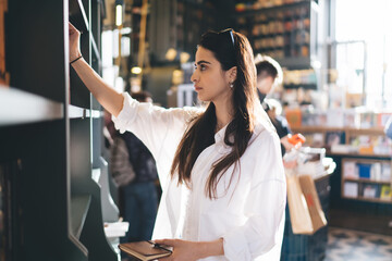 Focused woman taking book from bookshelf