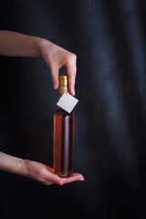 female hands holding 250 ml bottle of pink wine with mock up label, no brand on black background. Alcohol drink, copy space