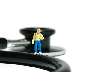 Miniature people toy figure photography. A boy kindergarten student standing above stethoscope. Isolated on white background.