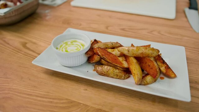 Professional kitchen sour cream sauce and baked potato wedges with spices in a plate on the table