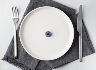 One blueberry on a white plate is the concept for any kind of diet and healthy eating. Top view, flat lay