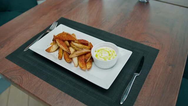 Restaurant dish sour cream sauce and baked potato wedges with spices in a plate on the table