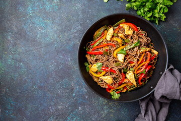 Japanese dish buckwheat soba noodles with chicken and vegetables carrot, bell pepper and green beans in wok on dark blue background