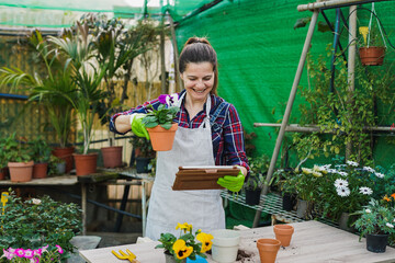 Mature woman working inside garden greenhouse while using digital tablet - Harvest and plant nursery concept