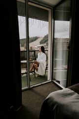 A woman in a white bathrobe eats a croissant and drinks coffee in a hotel in the mountains.Resort vacation concept