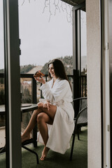 Fototapeta na wymiar A woman in a white bathrobe eats a croissant and drinks coffee in a hotel in the mountains.Resort vacation concept
