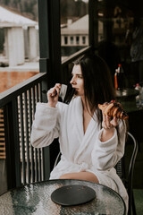 A woman in a white bathrobe eats a croissant and drinks coffee in a hotel in the mountains.Resort vacation concept