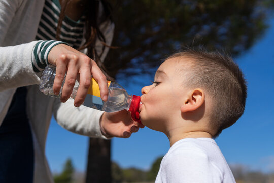 Kid drinking water from bottle by help of mother