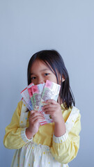 Asian young girl feel happy and holding some money of Indonesian rupiah. Concept of receiving THR on Eid al-Fitr or Lebaran days for muslim.