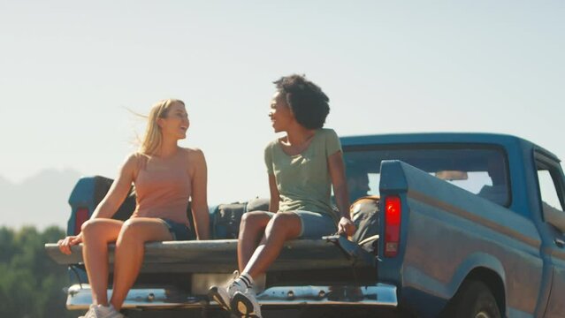 Two women riding in back of pick up truck as friends enjoy road trip through countryside - shot in slow motion