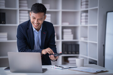 Portrait of Smiling young male employee feel euphoric with promotion offer in paperwork letter in office. a cheerful man sitting at his desk using smart phone at home office.