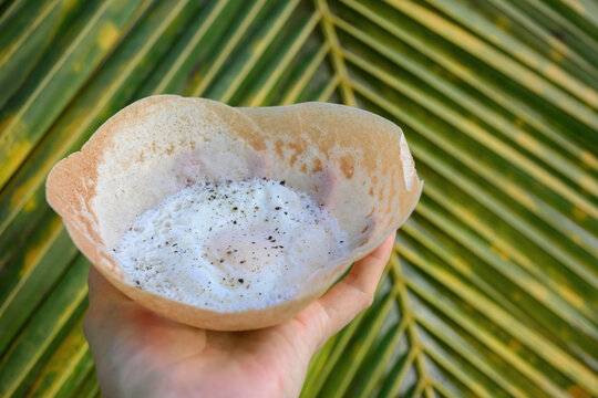 Sri lankan street food egg hopper in woman's hand for breakfast. Close up. Local food. Outdoors. bittara appa.