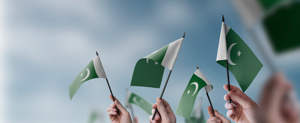 A group of people holding small flags of the Pakistan in their hands - obrazy, fototapety, plakaty