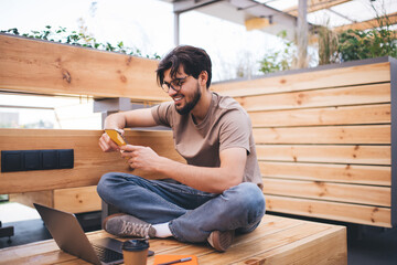 Smiling young man sitting with smartphone on terrace