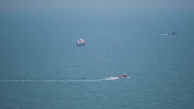 Handheld shot of tourists enjoying parasailing from the boat at Vagator beach in Goa, India. Adventure activities in Goa. Tourist experiencing parasailing in the middle of the sea from boat. 