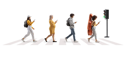 Full length profile shot of young people crossing street at a pedestrian crossing and using mobile phones