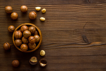 Wooden bowl of raw macadamia nuts in shell. Healthy protein snack background