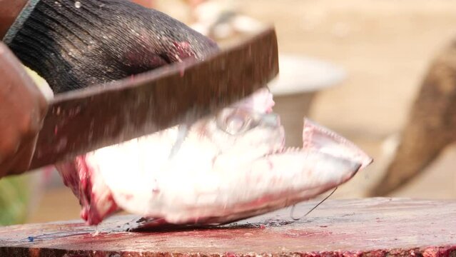 A man using a cutlass to remove the head of a fresh fish, cutting it's mouth first
