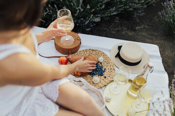Woman have picnic outside. Lady in summer dress eat croissant and drink white wine.