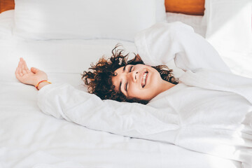 Beautiful cheerful woman in a white bathrobe lying on the bed in the morning.