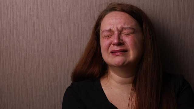 Distressed woman bitterly cry near room wall. Tears roll down cheeks, tearful eyes and swollen face. Splash out emotions, sob violently. Emotional breakdown, sufferings. Depression and hysterics.