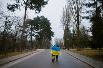 A couple walking away covered with Ukrainian flag. Ukrainian soldier and his wife with Ukrainian flag