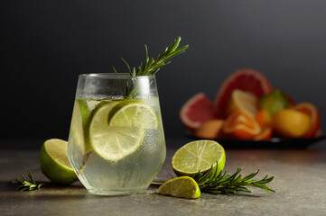 Cocktail gin tonic with ice, rosemary, and lime on a stone table.