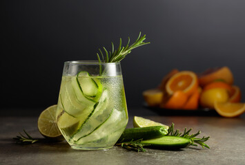 Cocktail gin tonic with ice, rosemary, lime, and cucumber on a stone table. - obrazy, fototapety, plakaty